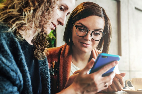 Jetzt Konto-Welt entdecken Zwei junge Leute schauen auf ein Smartphone