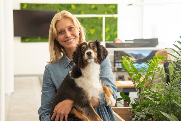Jetzt bewerben! Mitarbeiterin lächelt in die Kamera und hält ihren Hund auf dem Arm